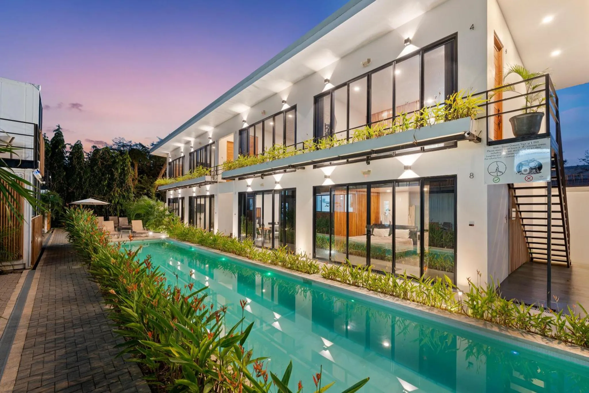Bâtiment moderne avec piscine et végétation luxuriante au crépuscule.