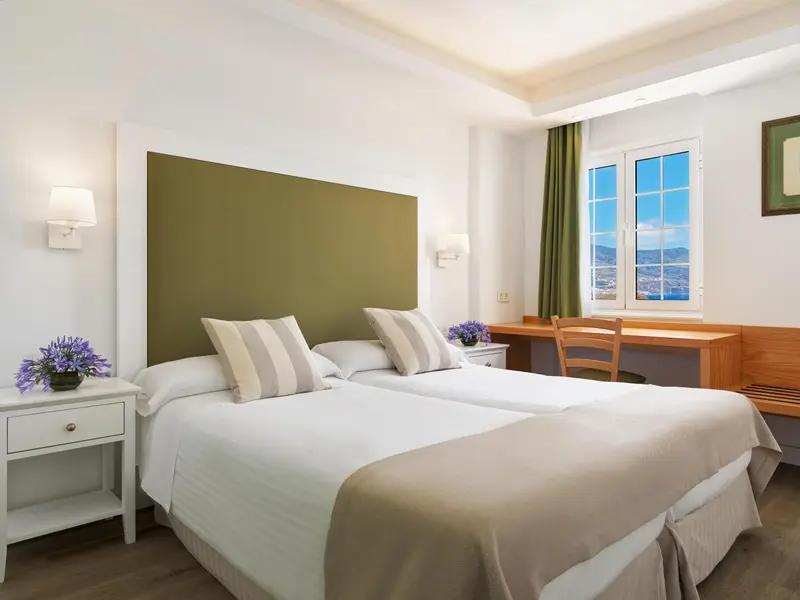 Une chambre lumineuse avec un grand lit et un bureau près de la fenêtre.