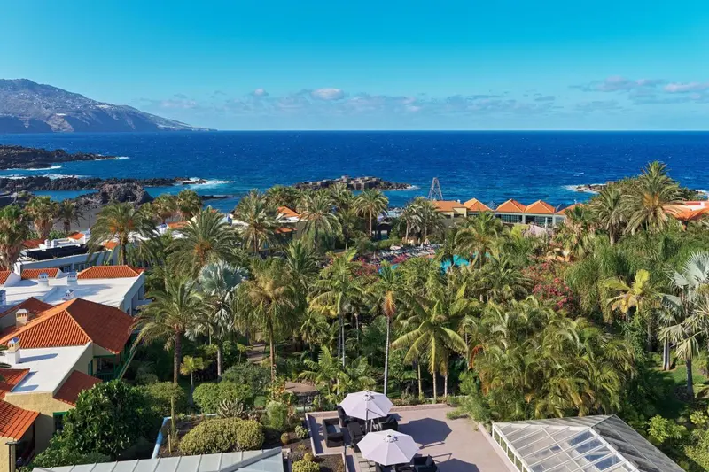Vue aérienne d'un complexe hôtelier tropical avec piscine et végétation luxuriante face à la mer.