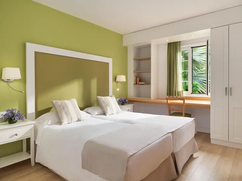 Une chambre lumineuse avec un lit double et un bureau près de la fenêtre.
