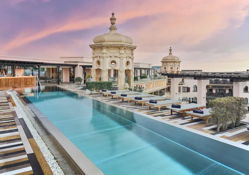 Piscine à débordement sur un toit-terrasse avec architecture ornementale et chaises longues.