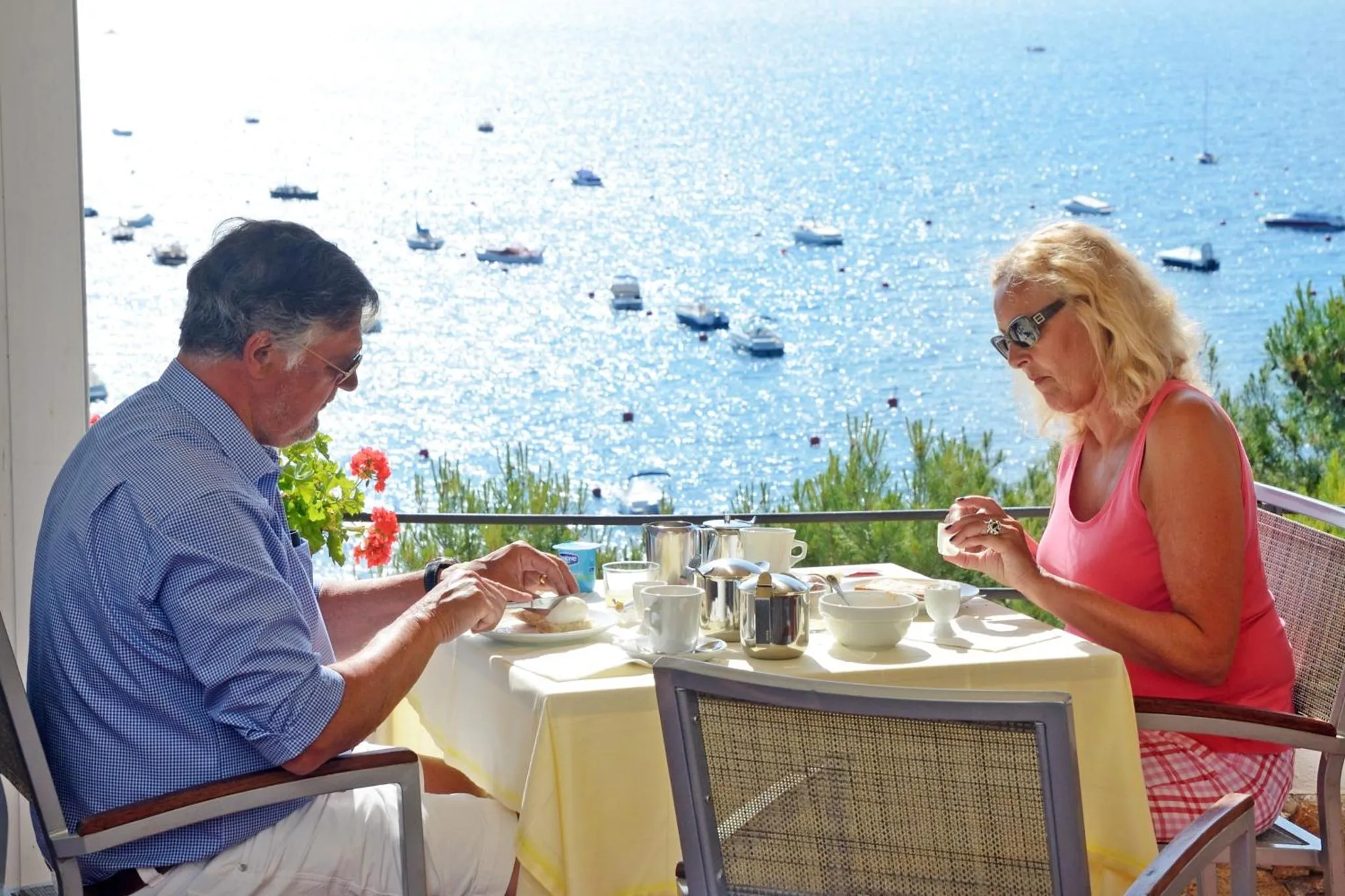 Un couple prend son petit-déjeuner sur une terrasse ensoleillée avec vue sur la mer.