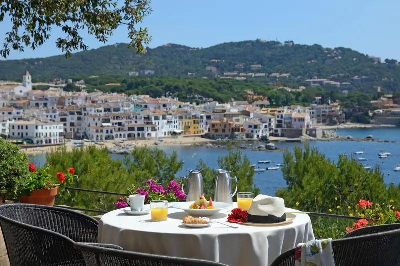 Une table est dressée pour le petit-déjeuner avec vue sur la mer et un village.