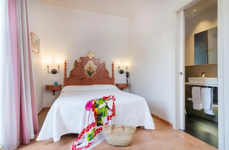 Une chambre lumineuse avec un lit recouvert d'une courtepointe blanche et un pan de rideau rose.