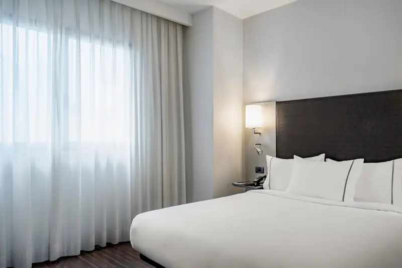 Une chambre d'hôtel lumineuse avec un grand lit et des rideaux blancs.