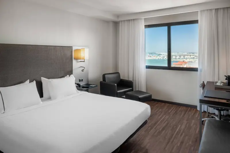 Une chambre d'hôtel lumineuse avec un lit double et un fauteuil près de la fenêtre.
