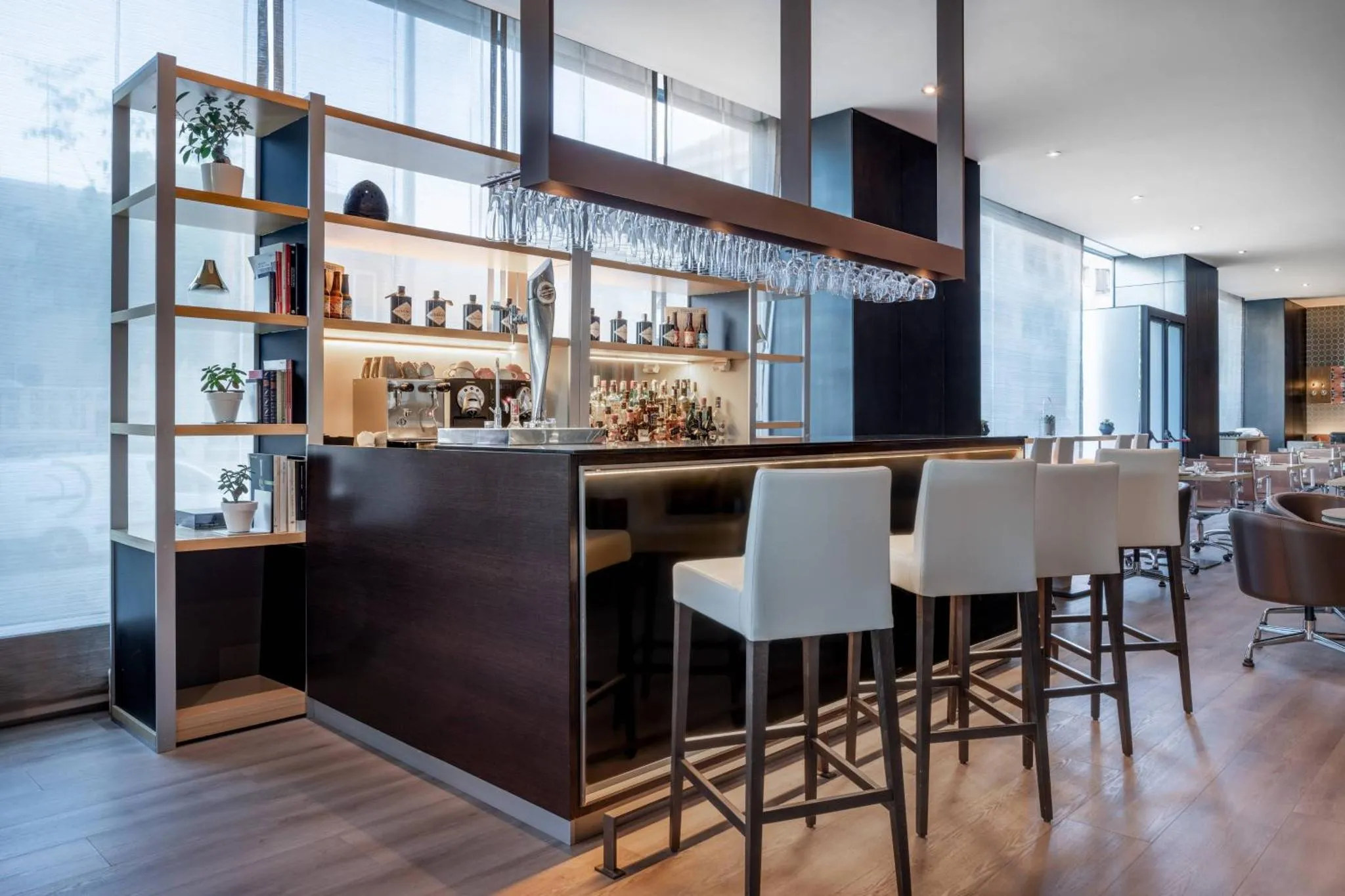 Un comptoir de bar moderne avec des tabourets et des étagères remplies de bouteilles et de verres.