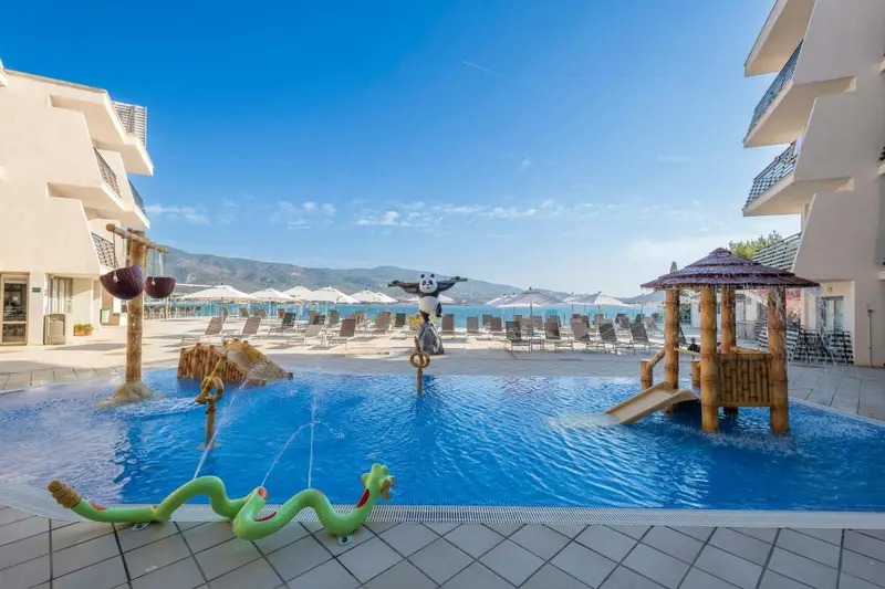 Piscine d'hôtel avec jeux d'eau et transats sur une terrasse ensoleillée.