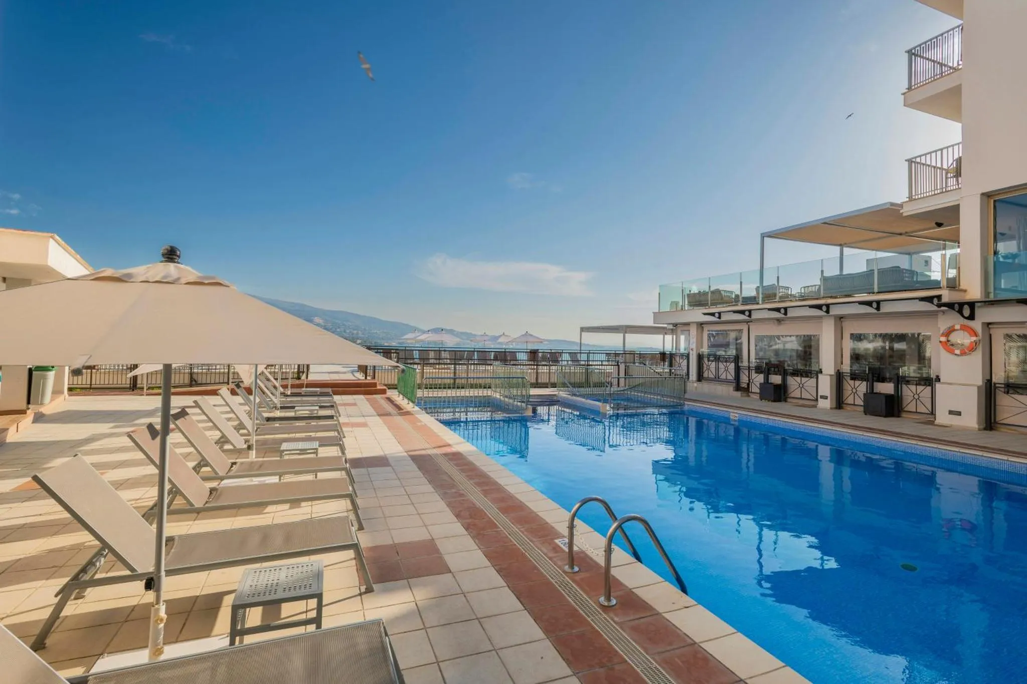 Terrasse avec transats et piscine au bord d'une vue sur la mer et les montagnes.