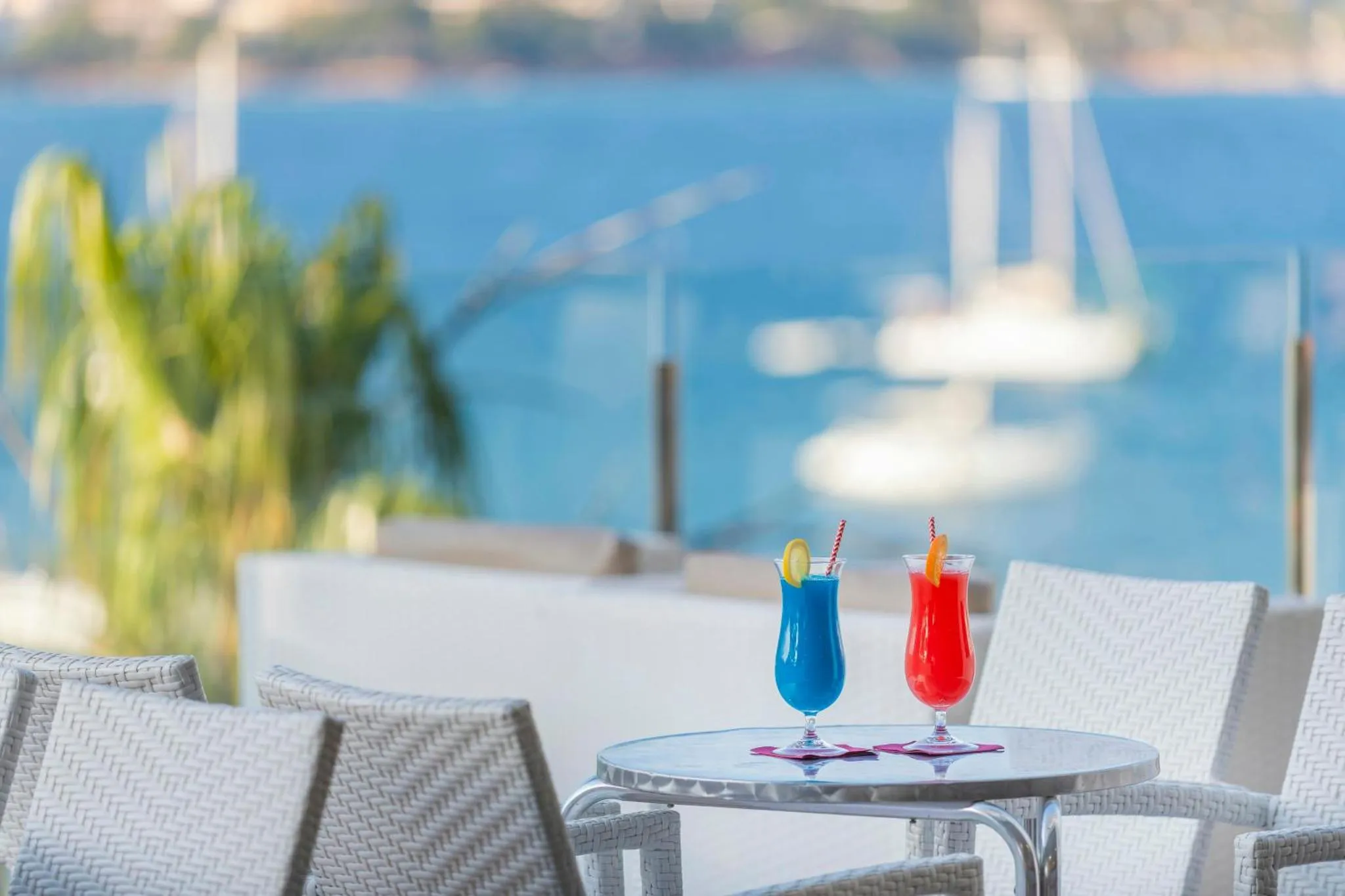 Deux cocktails colorés sur une table en terrasse avec vue sur la mer et des bateaux.