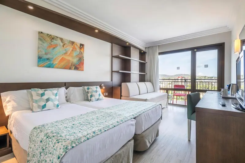 Chambre lumineuse avec un grand lit et un espace détente près d'une baie vitrée.