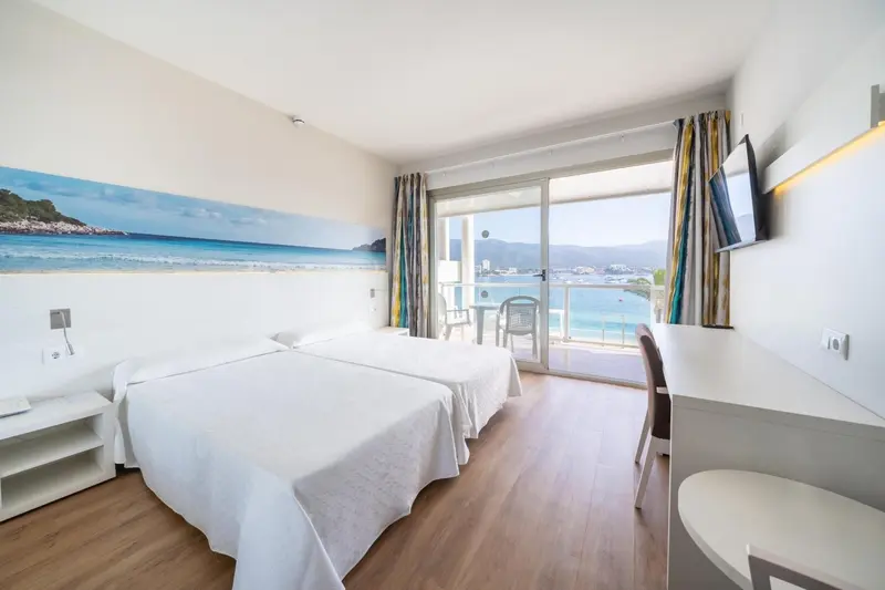 Chambre lumineuse avec vue sur la mer depuis un balcon.