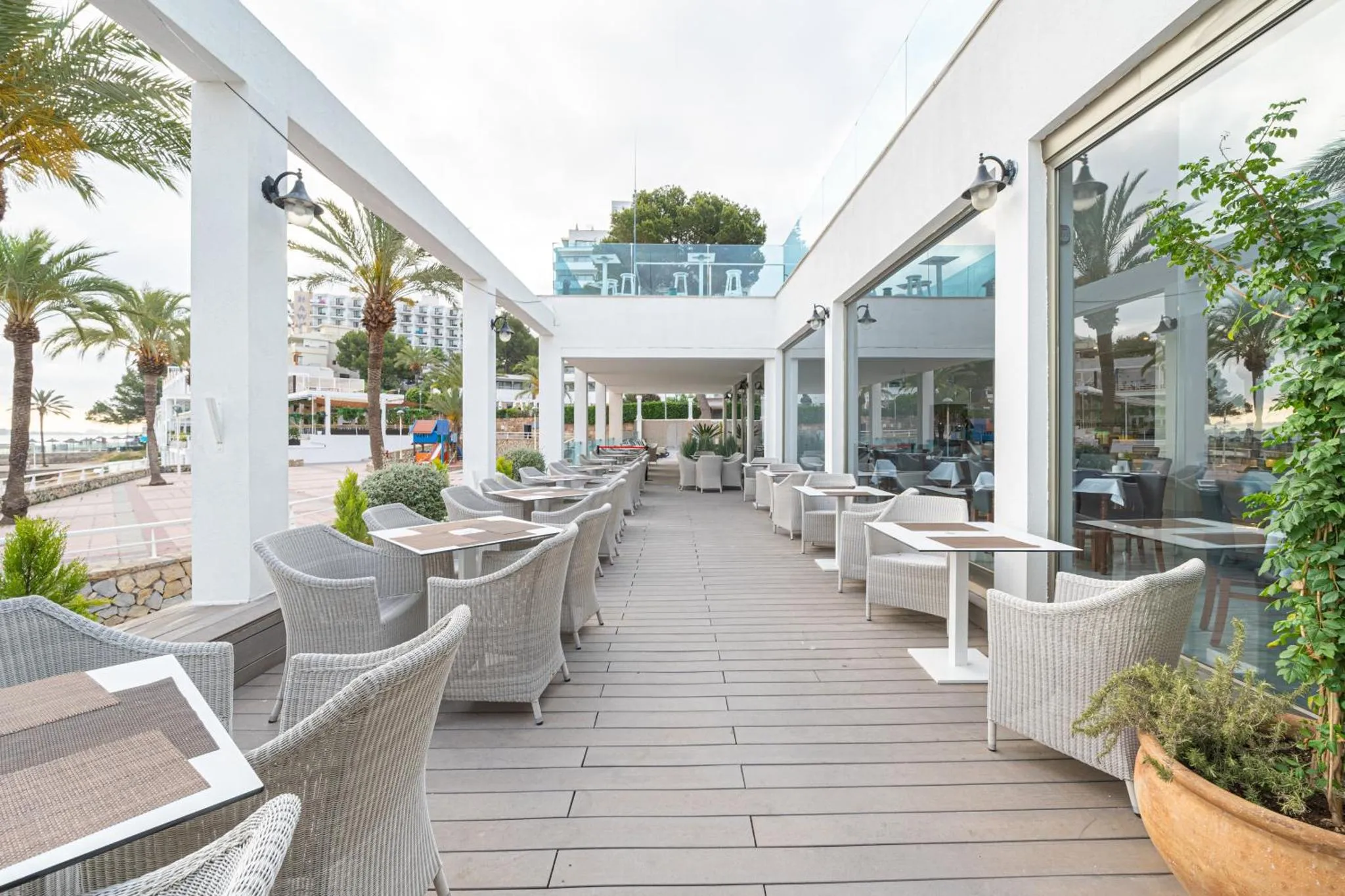 Terrasse ombragée avec tables et chaises en osier face à la mer.