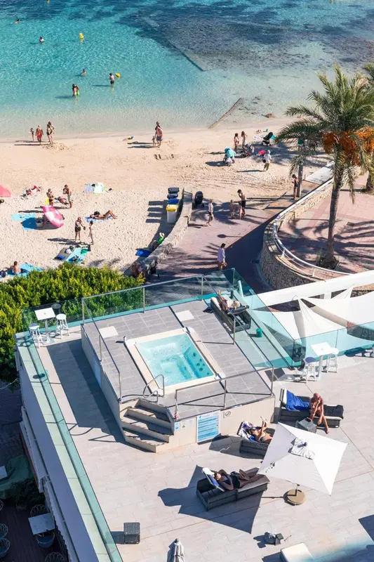 Vue aérienne d'une plage ensoleillée avec des transats et une piscine à débordement.