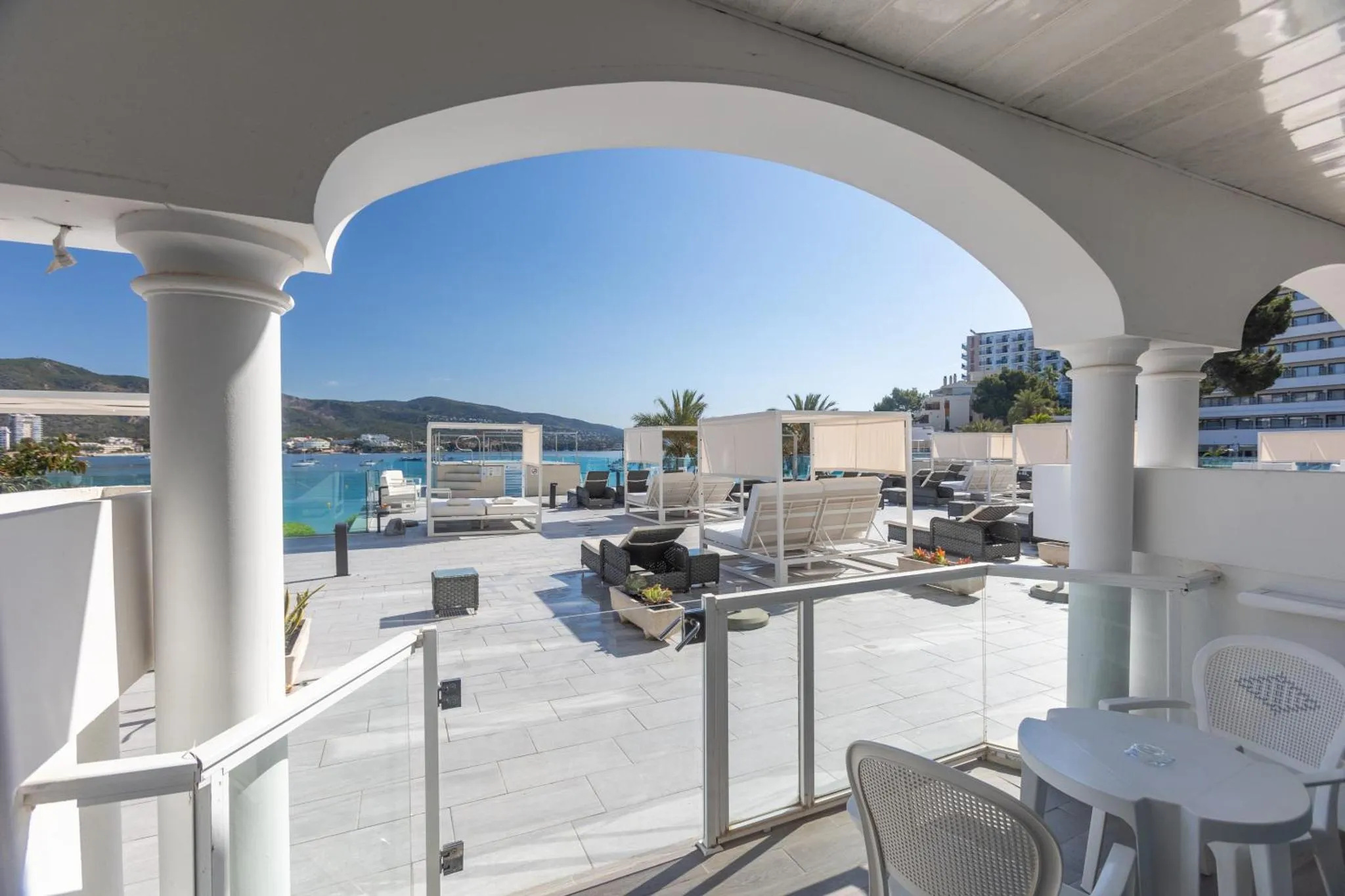 Vue sur une piscine et une terrasse ensoleillée depuis un balcon ombragé.