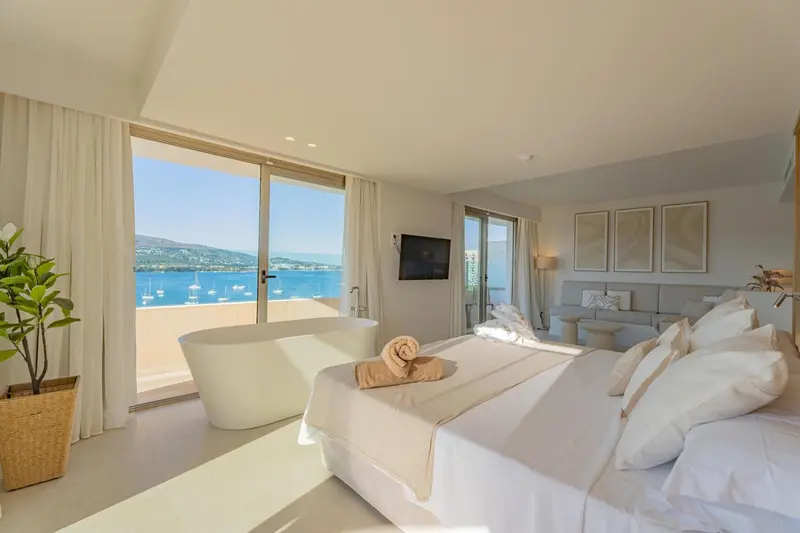Une chambre lumineuse avec un grand lit et une baignoire face à la mer.