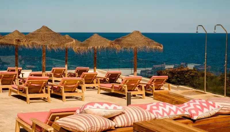 Terrasse ensoleillée avec transats et parasols vue sur la mer.