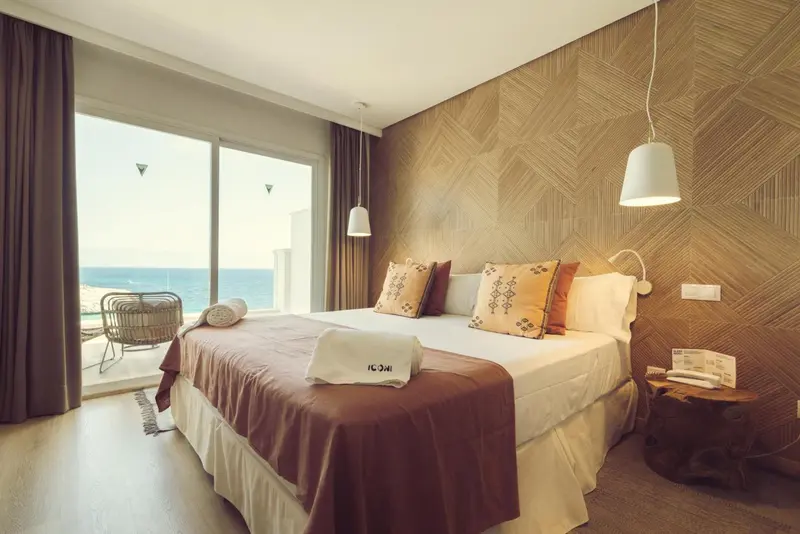 Une chambre avec un grand lit donnant sur la mer par de larges baies vitrées.