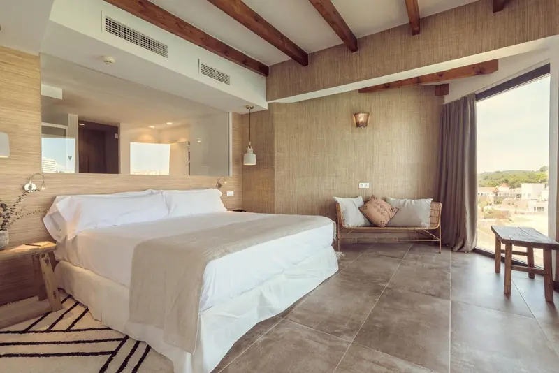 Une chambre lumineuse avec un grand lit et un coin salon près d'une fenêtre.
