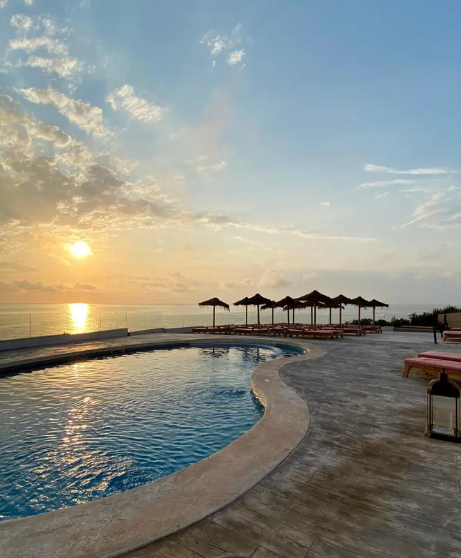 Une piscine bordée d'une terrasse avec des transats au coucher du soleil.
