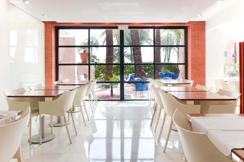 Une salle lumineuse avec des tables dressées face à une grande baie vitrée.