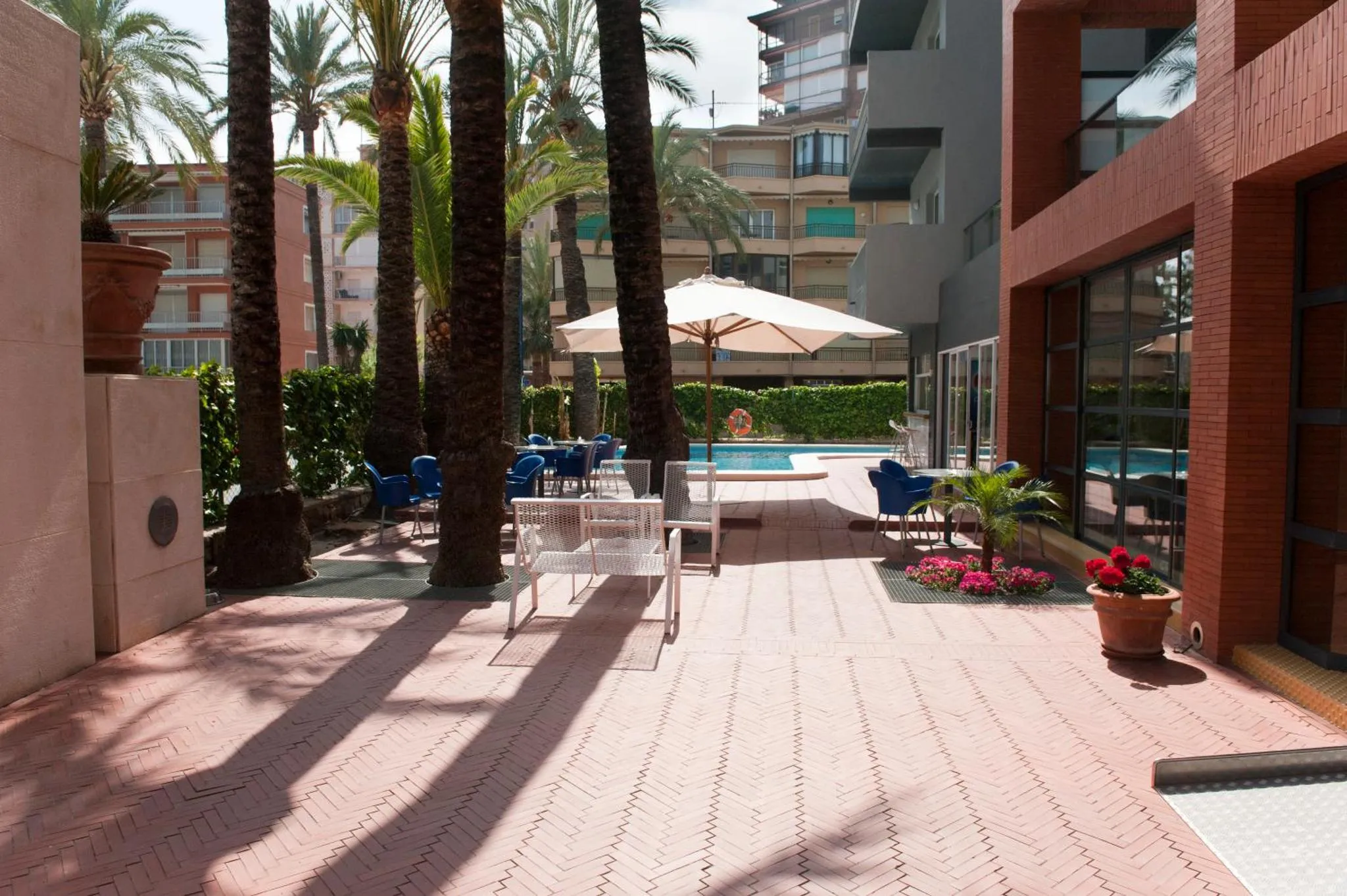 Terrasse ombragée avec tables et chaises près d'une piscine.