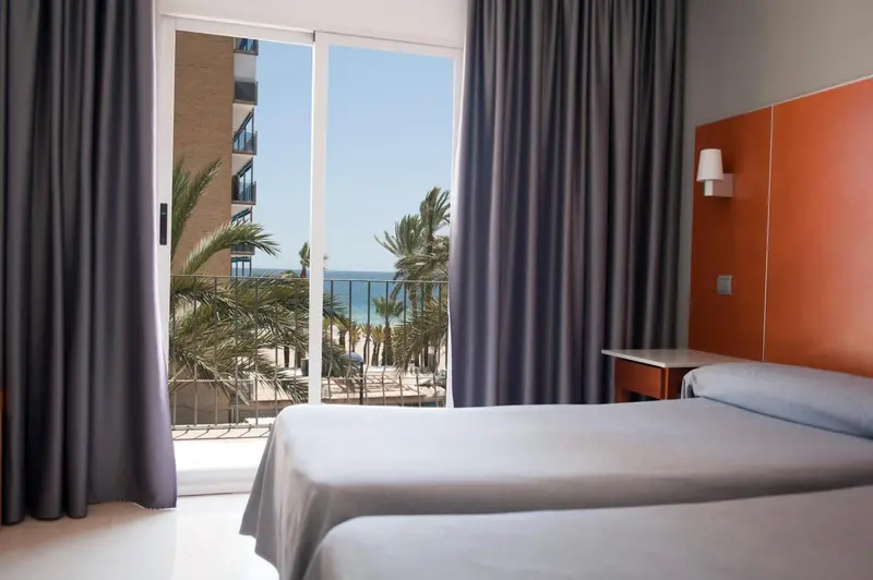 Une chambre lumineuse avec un grand balcon donnant sur la mer.