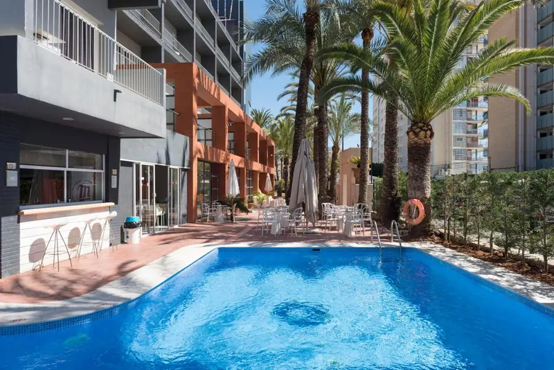 Une piscine turquoise bordée de chaises longues et de palmiers.