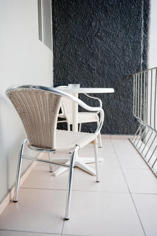 Une table et des chaises en osier blanc sur une terrasse carrelée.