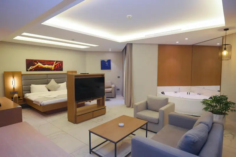 Une chambre lumineuse avec un grand lit, un coin salon et une baignoire jacuzzi.