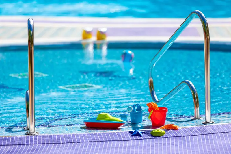 Une piscine turquoise avec des jouets et un escalier d'immersion.
