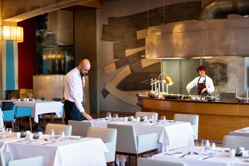 Une salle de restaurant lumineuse avec un comptoir de buffet et du personnel en cuisine.