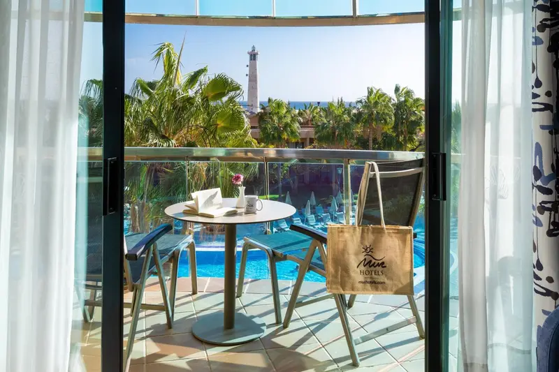 Une terrasse avec une table ronde et des chaises offre une vue sur la mer et un paysage urbain.