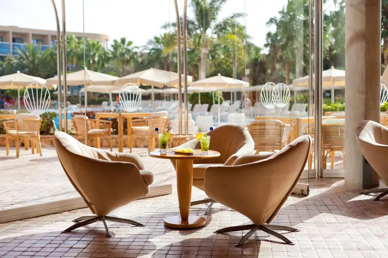 Espace de détente extérieur avec des fauteuils et des tables basses près d'une piscine.