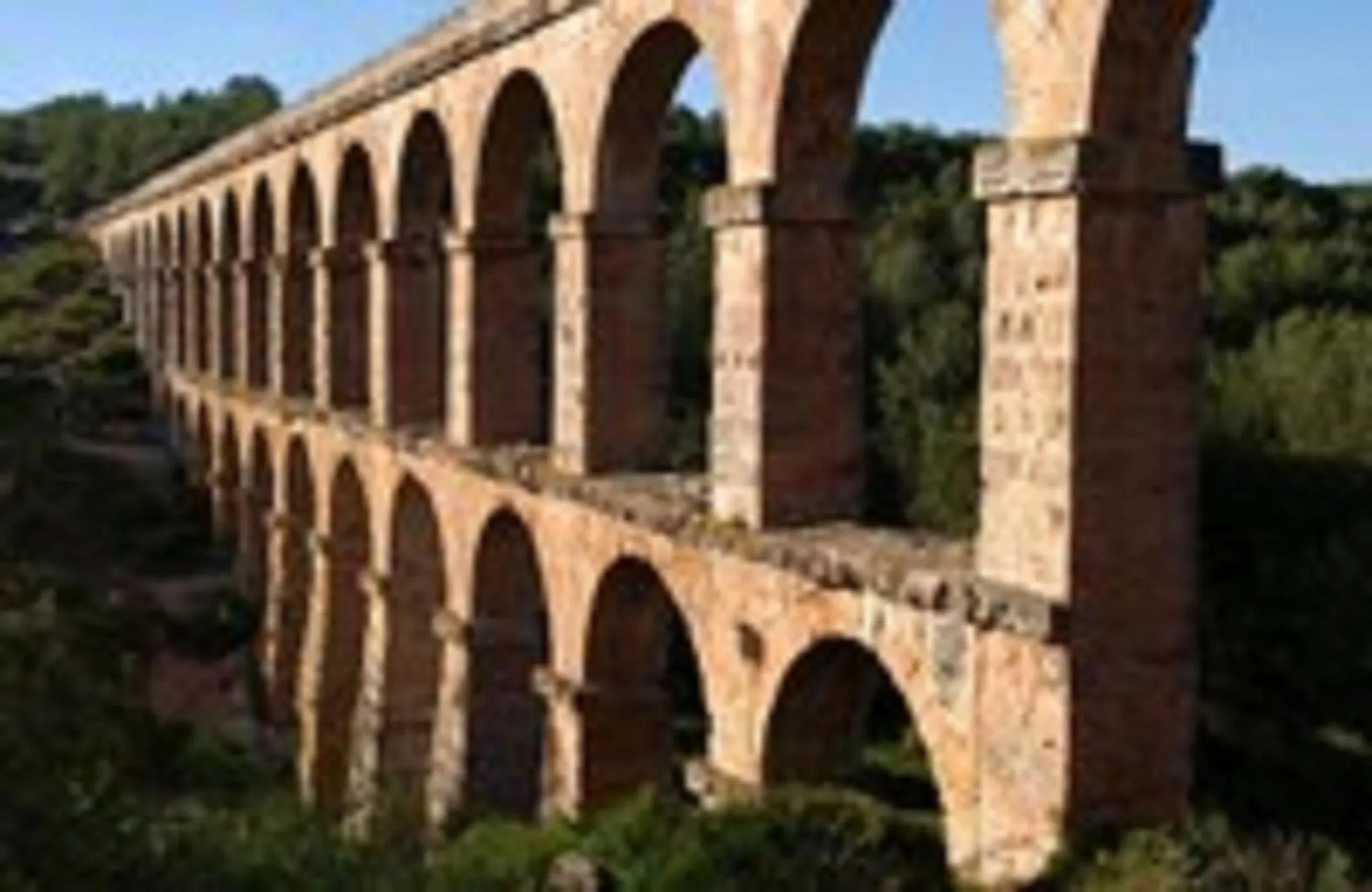 Long aqueduc en pierre avec de nombreuses arches s'étendant sur un paysage verdoyant.