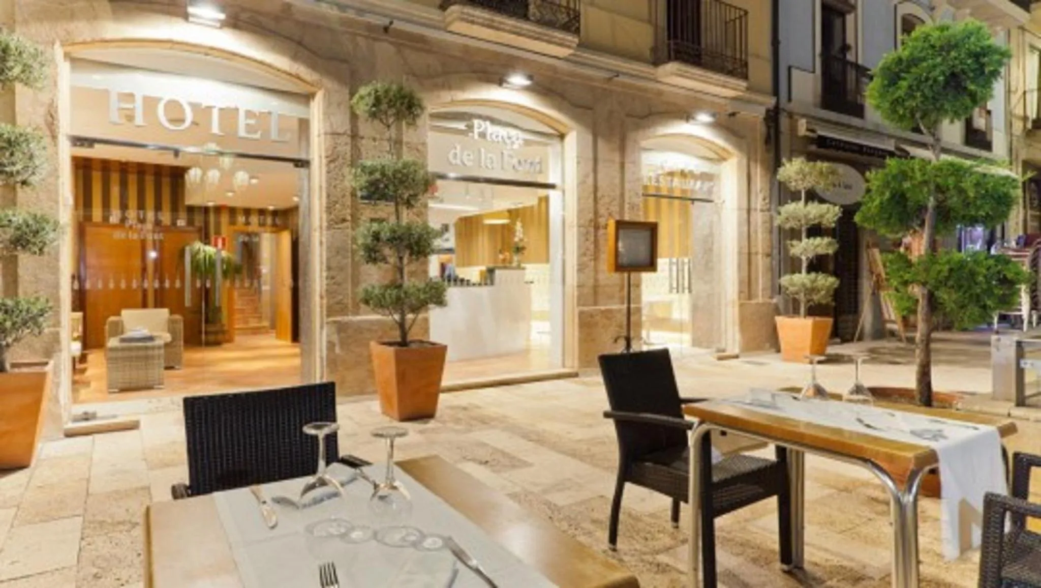 Façade d'hôtel avec tables de restaurant en terrasse.