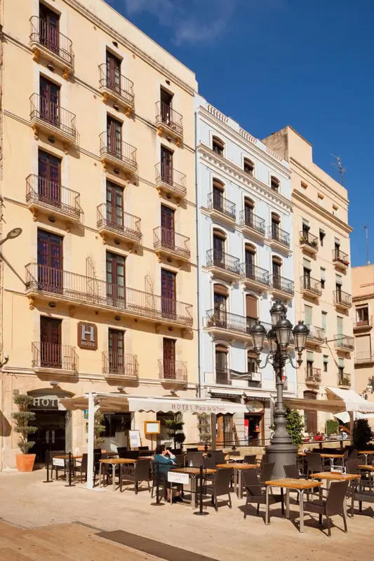 Façade d'un bâtiment à plusieurs étages avec des balcons et un café en terrasse.