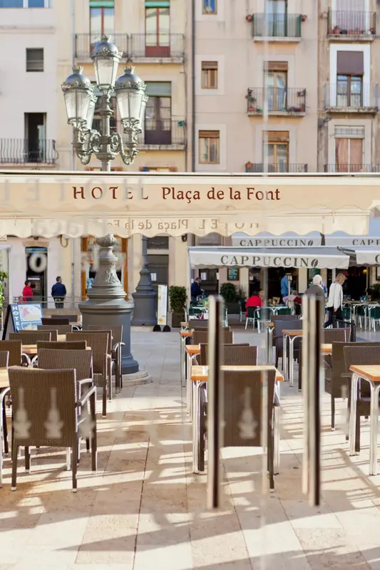 Terrasse de café ensoleillée devant un bâtiment à l'architecture classique.