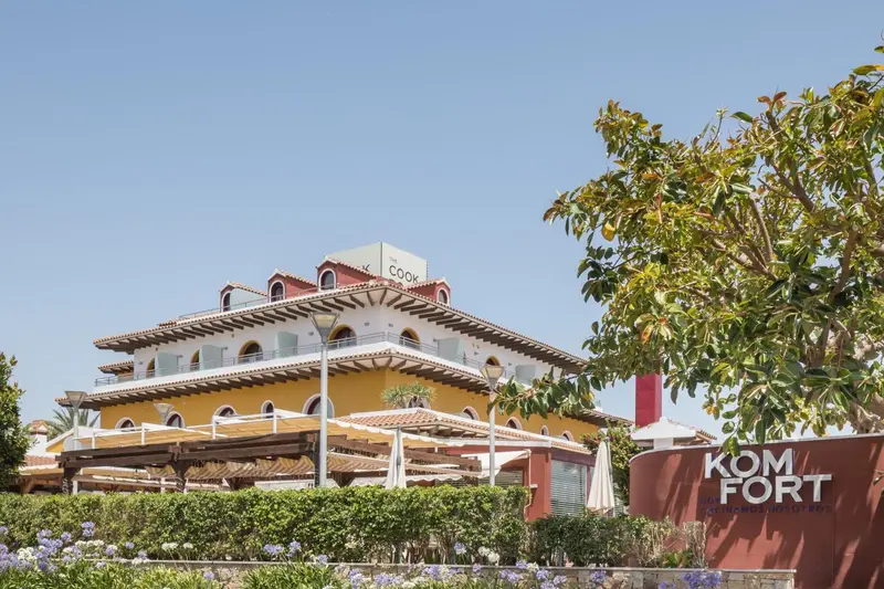 Bâtiment jaune et rouge avec des terrasses et une pergola ombragée.