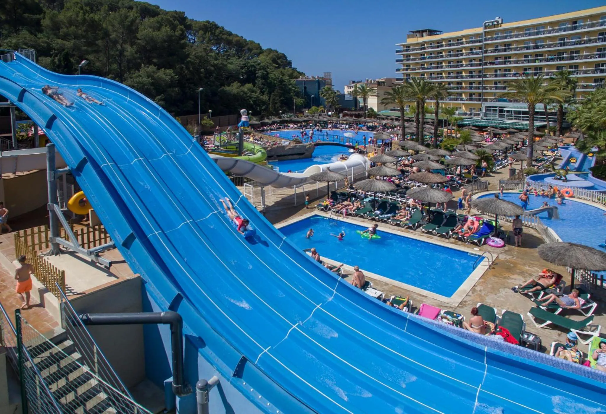 Toboggan aquatique bleu descendant vers une piscine ensoleillée avec des transats.