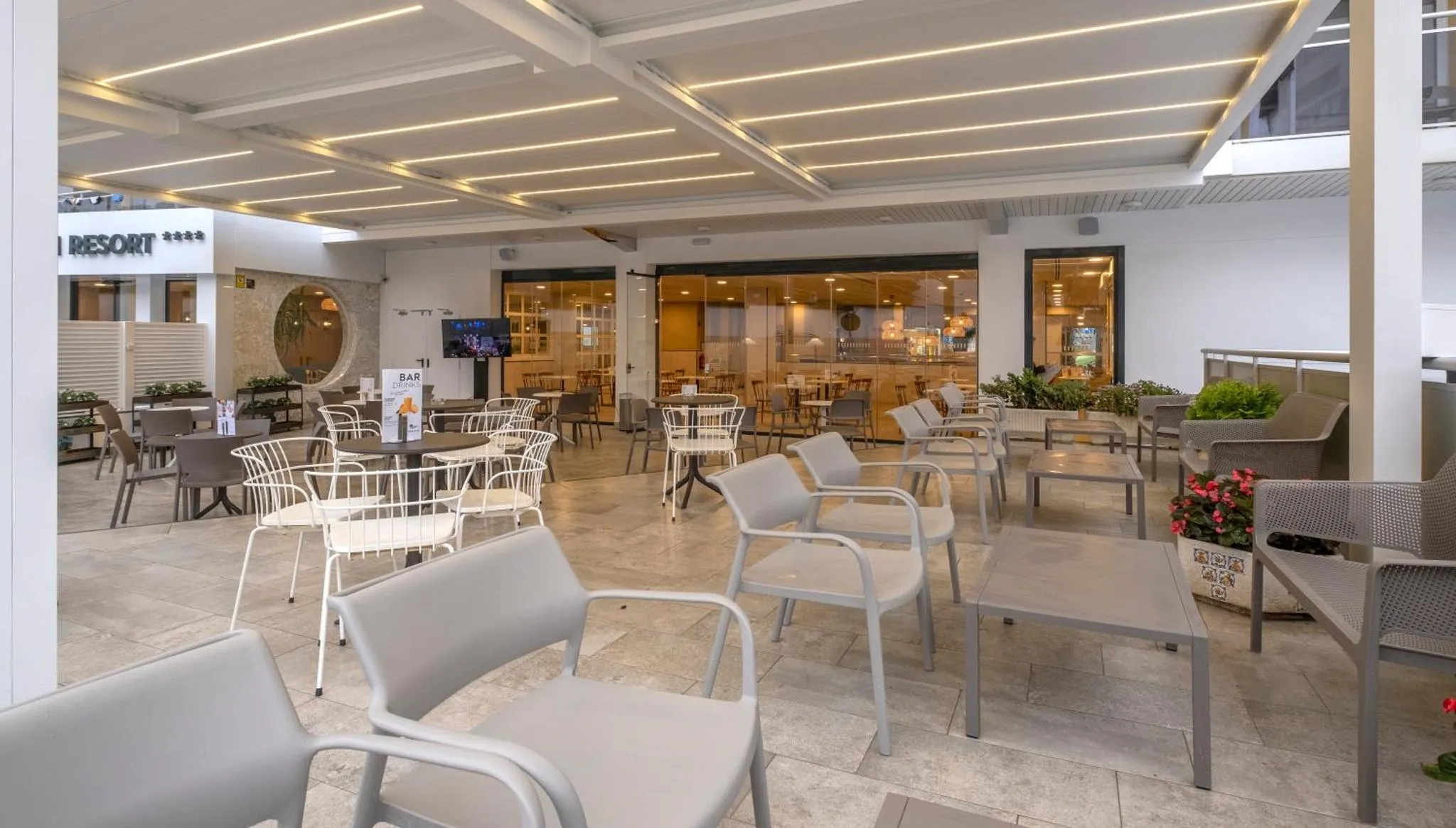 Terrasse ombragée avec tables et chaises, donnant sur un espace intérieur lumineux.