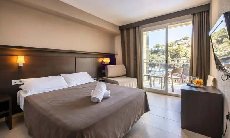 Une chambre avec un grand lit et un accès à une terrasse ensoleillée.