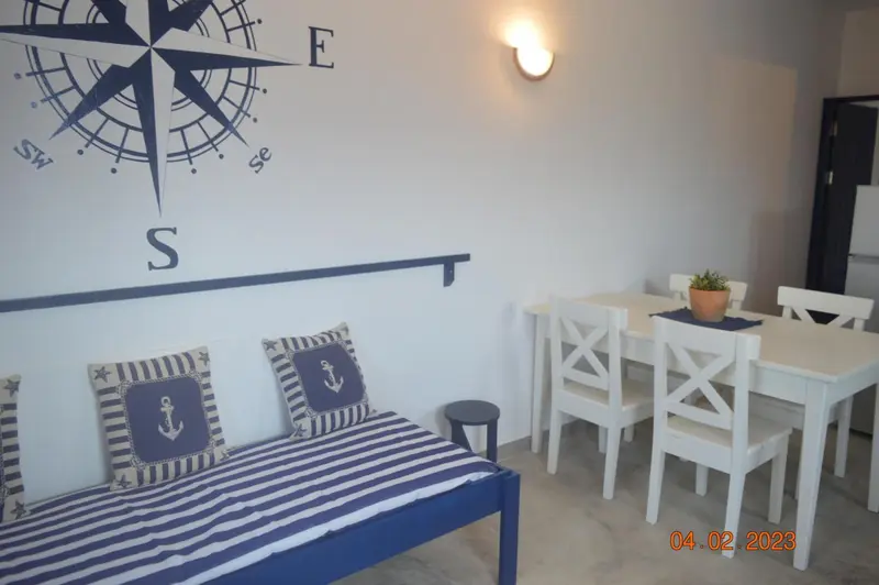 Une banquette rayée face à une table et des chaises blanches dans une pièce décorée d'une rose des vents.