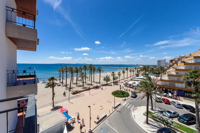 Vue aérienne sur une plage de sable fin bordée de palmiers et de bâtiments.