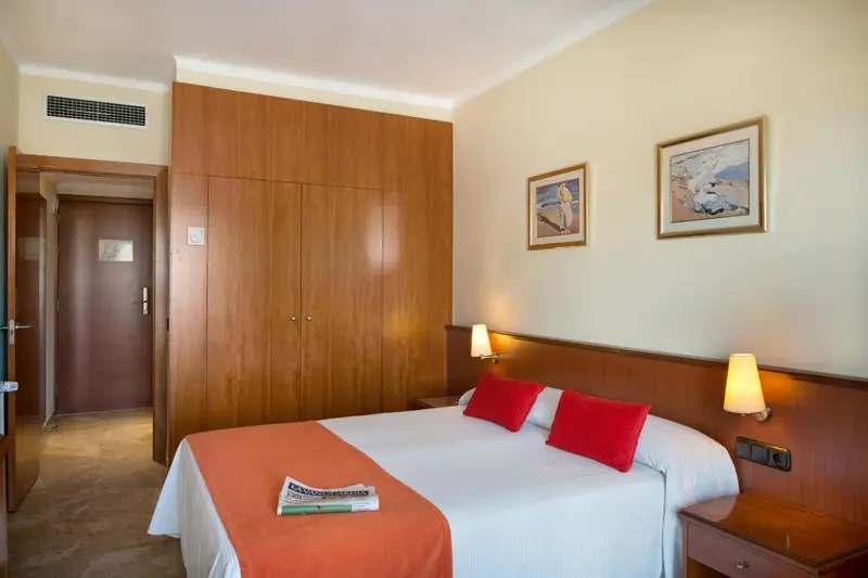 Une chambre lumineuse avec un grand lit recouvert d'une courtepointe orange et de coussins rouges.