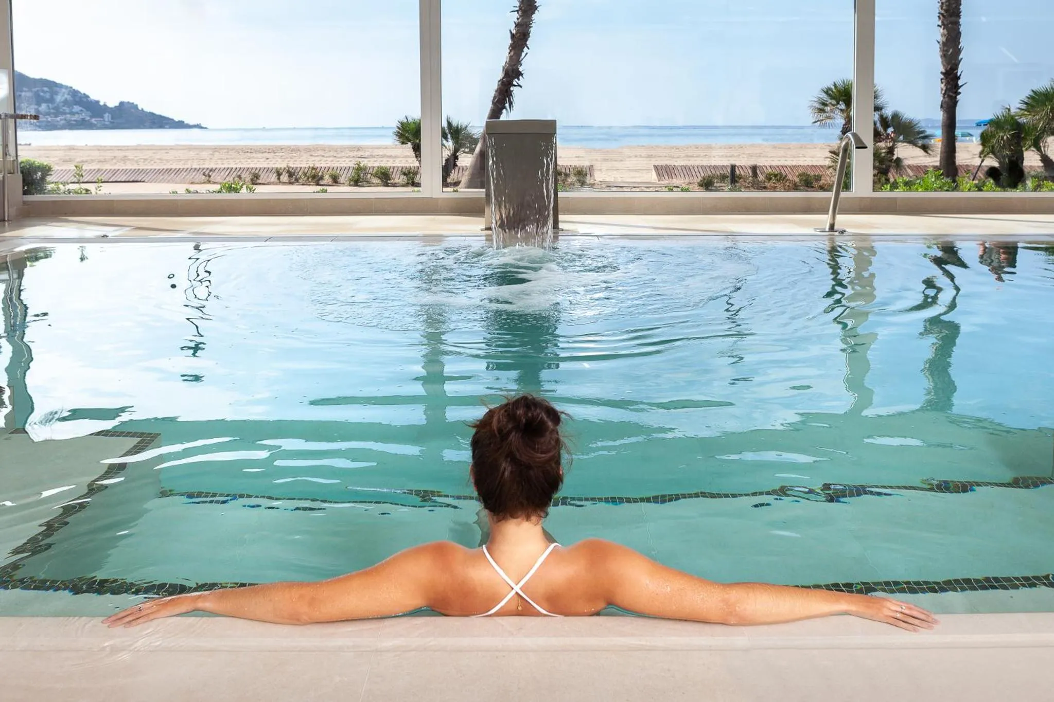 Une personne se détend dans une piscine intérieure avec vue sur la mer.
