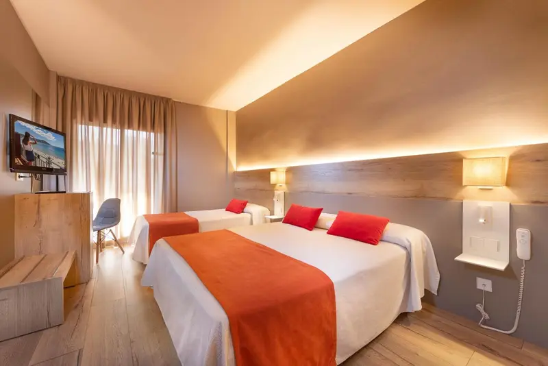 Chambre lumineuse avec deux lits simples et une télévision murale.