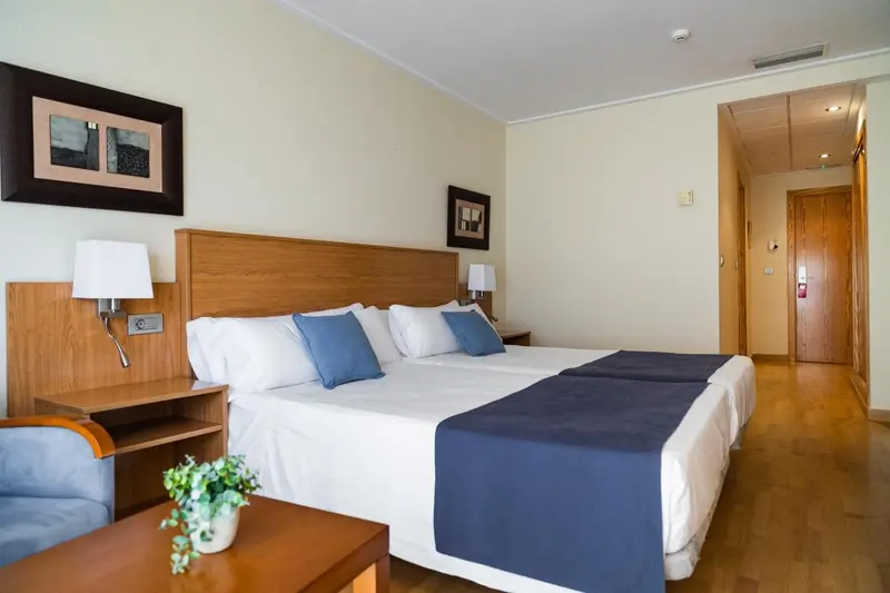 Une chambre lumineuse avec un grand lit recouvert d'une courtepointe blanche et de coussins bleus.