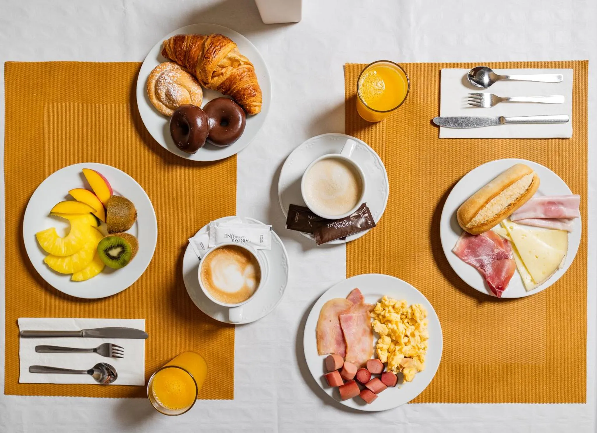 Un petit-déjeuner copieux est présenté sur une table recouverte d'une nappe jaune et orange.