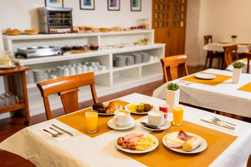 Une table est dressée pour le petit-déjeuner avec des viennoiseries, des fruits et des boissons.